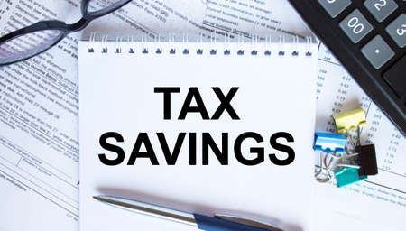 Notepad with text Tax Savings, paper clips, blue pen, eyeglasses on financial diagrams. Business conceptの写真素材