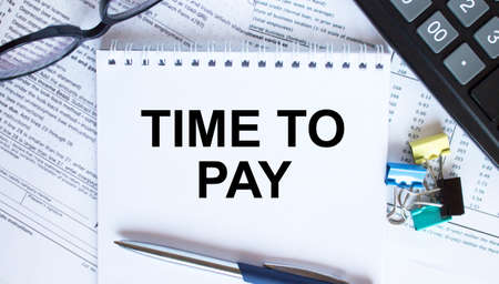 Notepad with text Time To Pay, paper clips, blue pen, eyeglasses on financial diagramsの写真素材