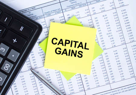 Sticker with text Capital Gains lying on the financial tables. Calculator with metal penの写真素材
