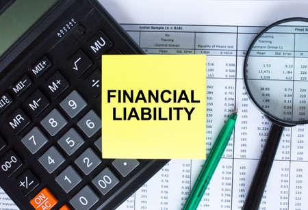 Sticker with text Financial Liability lying on the calculator. Magnifying glass with green pen on financial documents. Business and financial conceptの写真素材