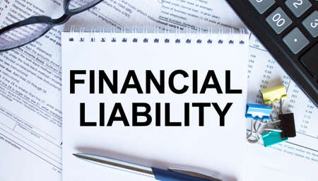 Notepad with text Financial Liability, paper clips, blue pen, eyeglasses on financial diagrams. Business conceptの写真素材