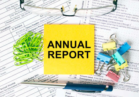 Orange sticker with text Annual Report. Next to it is a blue pen with colored stationery clips, green paper clips and eyeglasse. It can be used as a business and financial conceptの写真素材