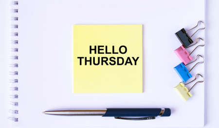 Yellow sticker with text Hello Thursday lying on a white Notepad with a pen and paper clips. Concept pgotoの写真素材
