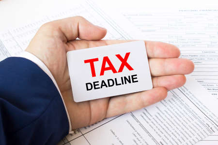 A man's hand is on the financial tables holding a business card with the inscription Tax Deadline. Business concept photoの写真素材