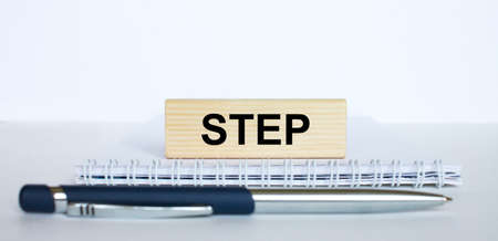 The word Step on a bar of wood, lying on a Notepad with a metal blue pen. Business concept photoの写真素材