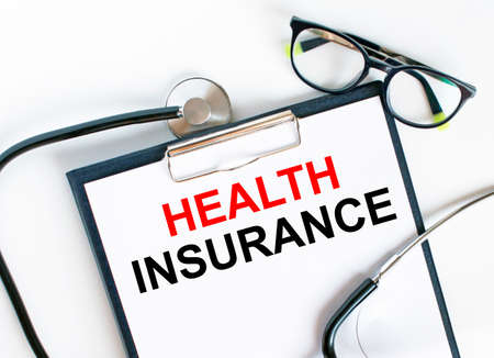 Text Health Insurance in the folder with the stethoscope and glasses. Medical concept photoの写真素材
