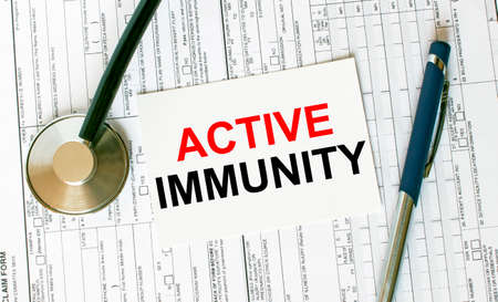 Text Active Immunity on the white card with the stethoscope, pen and medical documents. Medical concept photoの写真素材