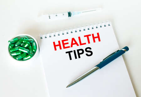 Text Health Tips written in a notebook with a blue pen and a bunch of pills. Can be used as a medical conceptの写真素材