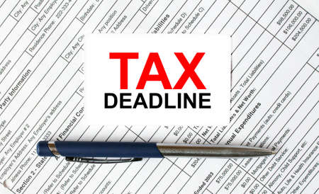 Text Tax Deadline written on a business card lying on financial tables with a blue metal pen. Business and financial conceptの写真素材