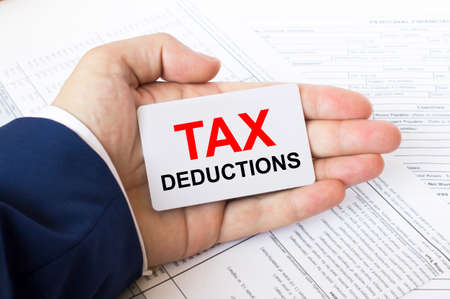 A man's hand is on the financial tables holding a business card with the inscription Tax Deductions. Business concept photoの写真素材