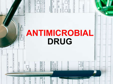 Text Antimicrobial Drug on the white card with the stethoscope, pen, green pills and medical documents. Medical concept photoの写真素材