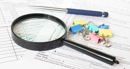 There are a lot of paper clips with a magnifying glass and a pen on the financial documents. Can be used as a concept photoの写真素材