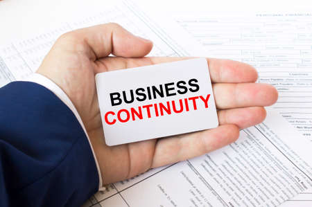 A man's hand is on the financial tables holding a business card with the inscription Business Continuity. Business concept photoの写真素材