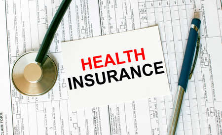 Text Health Insurance on the white card with the stethoscope, pen and medical documents. Medical concept photoの写真素材