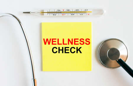 Yellow sticker with the text Wellness Check. A thermometer with a phonendoscope on a white background. Can be used as a medical concept photoの写真素材
