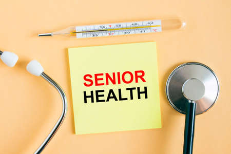 Yellow sticker with the text Senior Health. A thermometer with a phonendoscope on a warm background. Can be used as a medical concept photoの写真素材