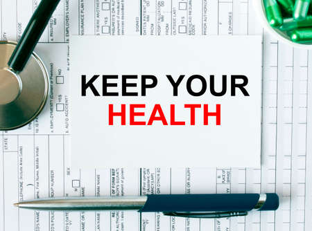 Text Keep Your Health on the white card with the stethoscope, pen, green pills and medical documents. Medical concept photoの写真素材