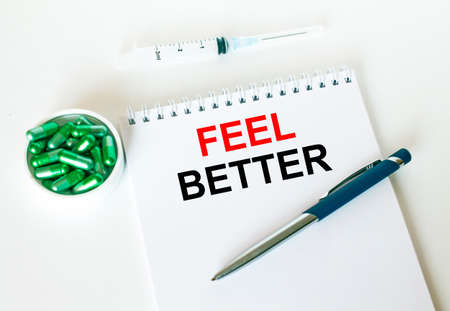 Text Feel Better written in a notebook with a blue pen and a bunch of pills. Can be used as a medical conceptの写真素材