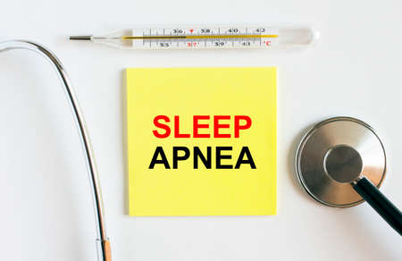 Yellow sticker with the text Sleep Apnea. A thermometer with a phonendoscope on a white background. Can be used as a medical concept photoの写真素材
