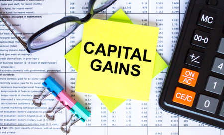 Text Capital Gains on yellow stickers with calculator, eyeglasses and paper clips. Business and financial conceptの写真素材