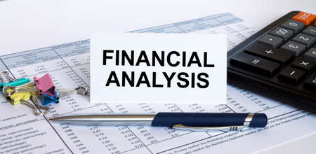 Text Financial Analysis on white card with blue metal pen, calculator and paper clips on financial table. Business and financial conceptの写真素材