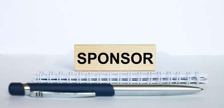 The word Sponsor on a bar of jenga wood, lying on a Notepad with a metal blue pen. Business concept photoの写真素材