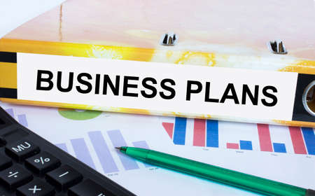 Text Business Plans on the folder that is located on the financial diagrams with green pen and calculator. Business and financial conceptの写真素材