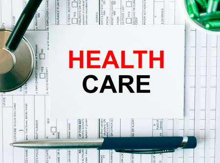 Text Health Care on the white card with the stethoscope, pen, green pills and medical documents. Medical concept photoの写真素材