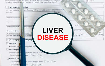 Magnifying glass with text Liver Disease inside lies on medical documents with pills and a blue metal pen. Can be use as a concept photoの写真素材