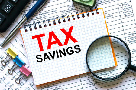 Text Tax Savings on notepad with calculator, clips, pen on financial report. Financial and business concept photoの写真素材