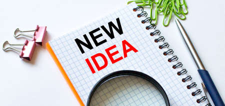 Notepad with text New Idea on white background with clips, pen and magnifying glass. Can be use as concept photoの写真素材