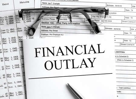Paper with text Financial Outlay on a financial table with eyeglasses and metal pen. Financial and concept photoの写真素材
