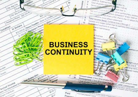 Orange sticker with text Business Continuity. Next to it is a blue pen with colored stationery clips, green paper clips and eyeglasse. It can be used as a business and financial conceptの写真素材