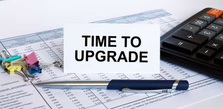 Text Time To Upgrade on white card with blue metal pen, calculator and paper clips on financial table. Business and financial conceptの写真素材