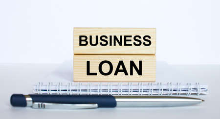 The text Business Loan on a bar of jenga wood, lying on a Notepad with a metal blue pen. Business concept photoの写真素材