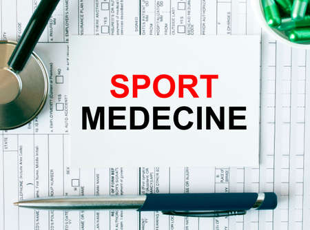 Text Sport Medecine on the white card with the stethoscope, pen, green pills and medical documents. Medical concept photoの写真素材