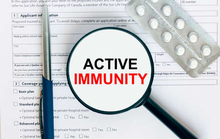 Magnifying glass with text Active Immunity inside lies on medical documents with pills and a blue metal pen. Can be use as a concept photoの写真素材