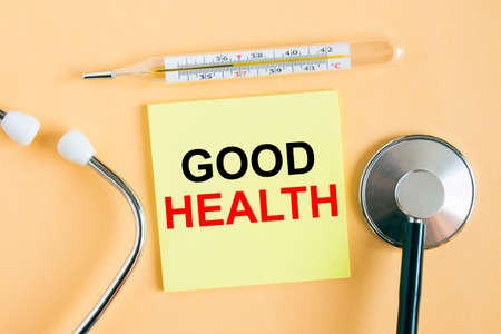 Yellow sticker with the text Good Health. A thermometer with a phonendoscope on a warm background. Can be used as a medical concept photoの写真素材