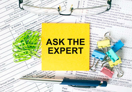 Orange sticker with text Ask The Expert. Next to it is a blue pen with colored stationery clips, green paper clips and eyeglasse. It can be used as a business and financial conceptの写真素材