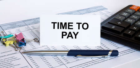Text Time To Pay on white card with blue metal pen, calculator and paper clips on financial table. Business and financial conceptの写真素材