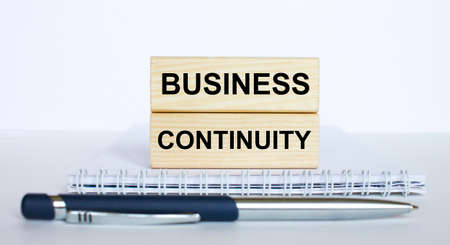 The text Business Continuity on a bar of jenga wood, lying on a Notepad with a metal blue pen. Business concept photoの写真素材