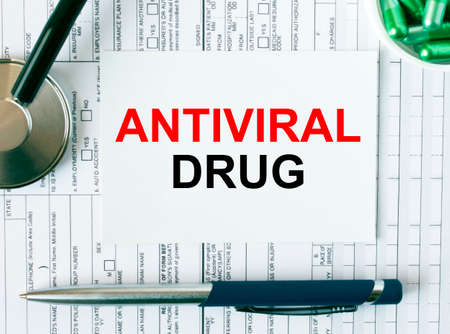 Text Antiviral Drug on the white card with the stethoscope, pen, green pills and medical documents. Medical concept photoの写真素材