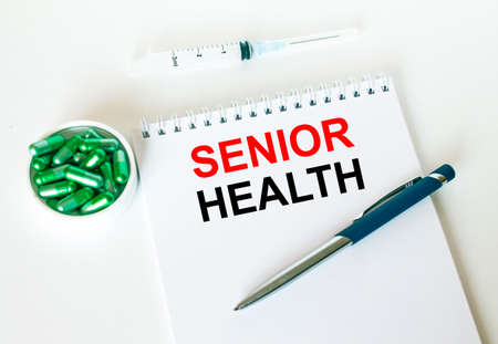 Text Senior Health written in a notebook with a blue pen and a bunch of pills. Can be used as a medical conceptの写真素材