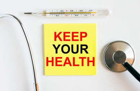 Yellow sticker with the text Keep Your Health. A thermometer with a phonendoscope on a white background. Can be used as a medical concept photoの写真素材