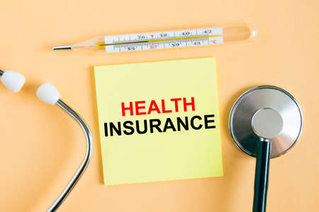 Yellow sticker with the text Health Insurance. A thermometer with a phonendoscope on a warm background. Can be used as a medical concept photoの写真素材