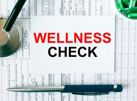 Text Wellness Check on the white card with the stethoscope, pen, green pills and medical documents. Medical concept photoの写真素材