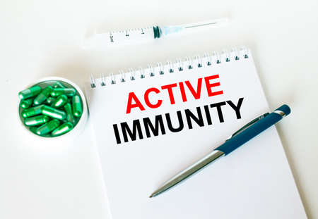 Text Active Immunity written in a notebook with a blue pen and a bunch of pills. Can be used as a medical conceptの写真素材