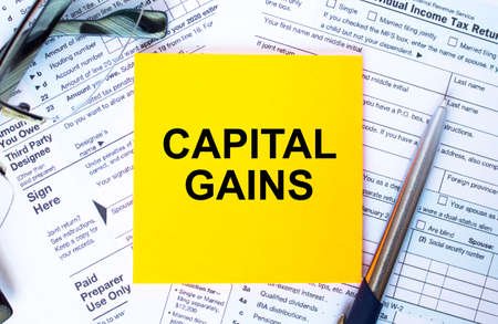 Financial concept. Text Capital Gains on note paper with the US IRS 1040 form, pen and glassesの写真素材