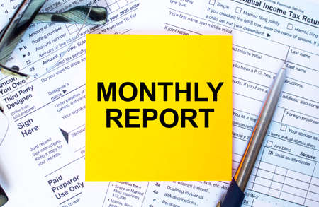 Financial concept. Text Monthly Report on note paper with the US IRS 1040 form, pen and glassesの写真素材
