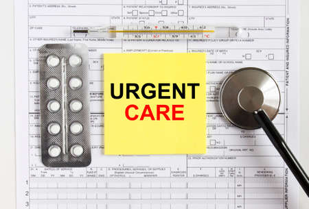 Text Urgent Care on yellow sticker with a stethoscope and pills are on medical documents. Medical concept photoの写真素材